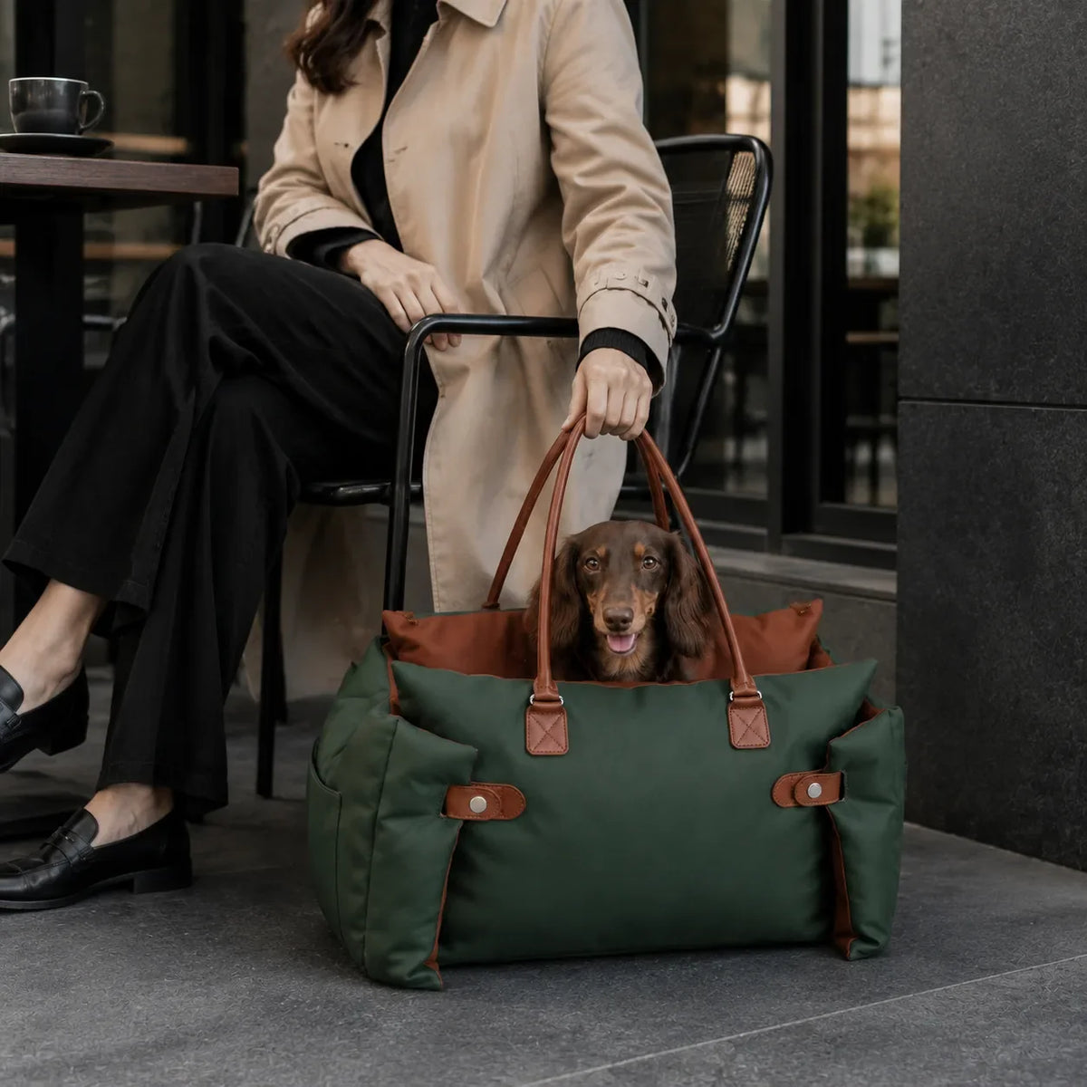 Woman holding a green pet carrier with a dachshund while seated outdoors